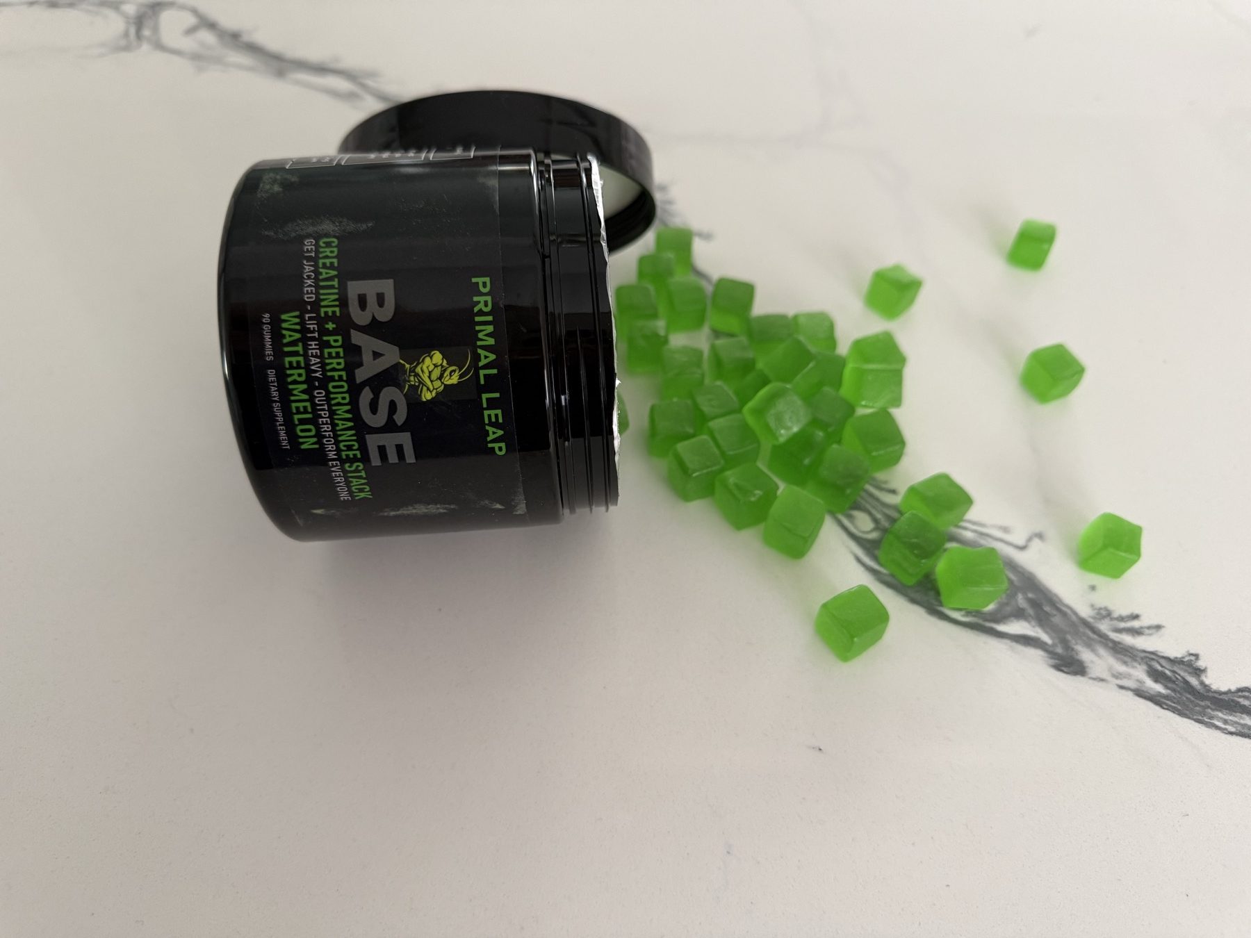 Smooth, glossy green BASE gummies spilling out of an open jar